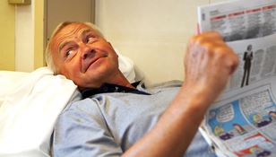 Mies lukee tyytyväisenä sanomalehteä laivan hytissä